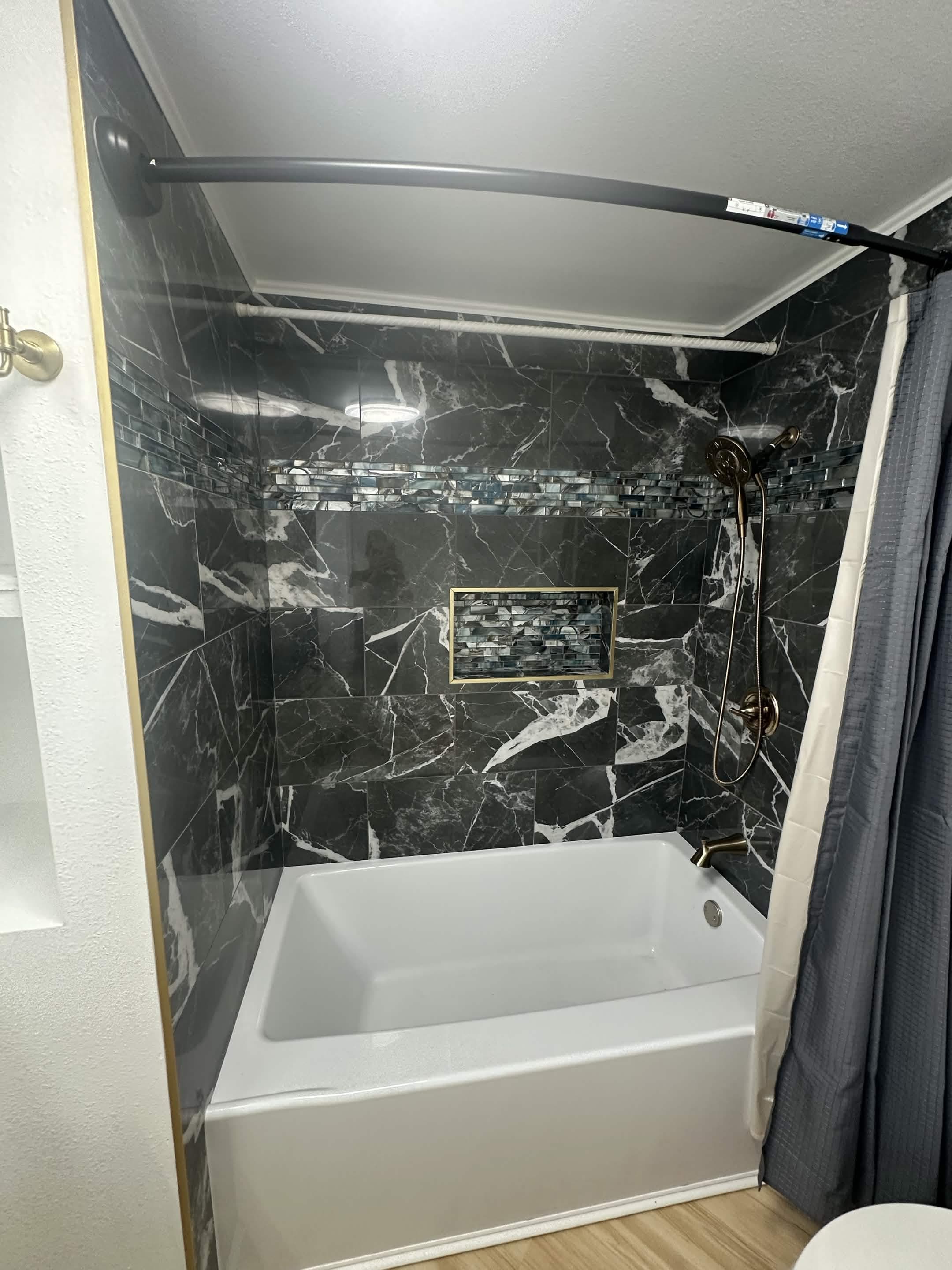 Black marble shower and tub surround with mosaic accent strip and bronze fixtures