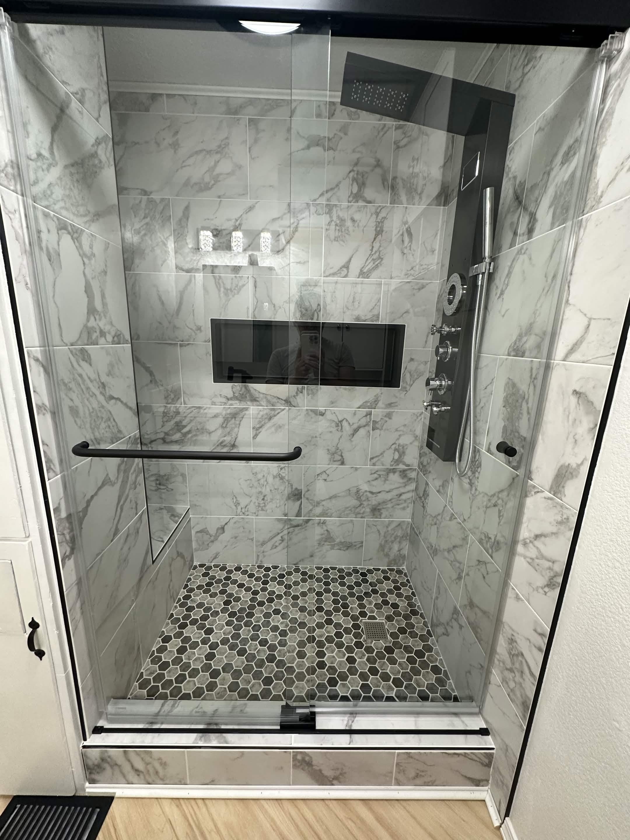 Close-up of walk-in shower with white marble tile, niche, and hexagon mosaic floor